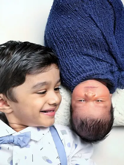 A playful pose with a smiling big brother looking at his newborn sibling from an inverted angle. It's a fun way to add some creativity to a sibling photoshoot.