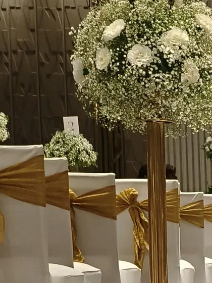 Another view of the classic white and gold seating arrangement. The large floral centerpieces and golden chair sashes add a touch of luxury and elegance to the reception hall.