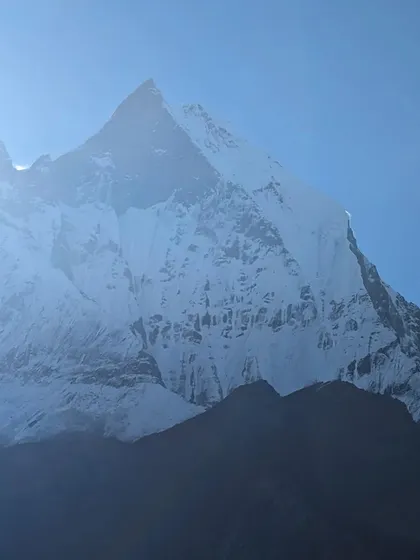 The sun creates a lens flare against the sharp silhouette of Machapuchare. The mountains inspire us to stand tall against all challenges.