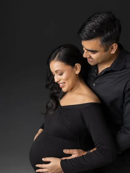 The beauty of simplicity. This close-up portrait against a dark grey background focuses on the couple's happy expressions as they embrace, capturing the intimacy of their pregnancy journey in a classic, all-black theme.