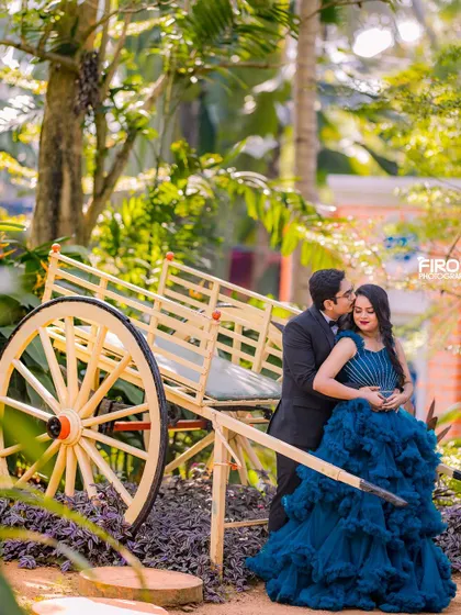 An intimate moment by a rustic bullock cart prop. The deep blue of the bride's gown contrasts beautifully with the natural wood and lush green surroundings.