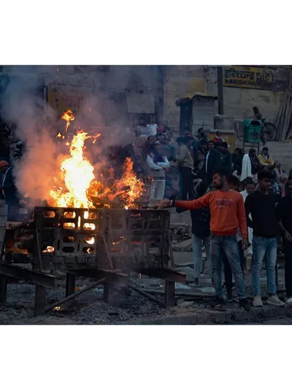 During the day, a crowd gathers around a burning pyre at the ghat. This image shows the communal nature of the rites, with family and workers present for the ceremony.