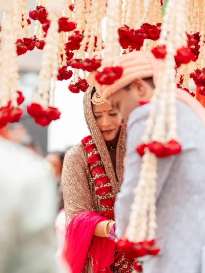 Sometimes, the most powerful moments are the most intimate. Framed by hanging garlands of red and white flowers, this emotional exchange between the couple captures the pure essence of their wedding day promises.