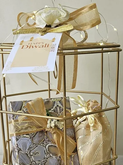A close-up of a golden birdcage hamper, beautifully wrapped and ready for gifting. It contains agate-print boxes and a delicate potli, making it a stylish and sophisticated Diwali present.