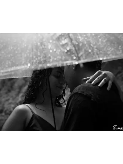 An intimate, close-up shot of a couple under an umbrella in the rain. This black and white photo focuses on their closeness and the texture of the raindrops, creating a very moody and romantic feel.