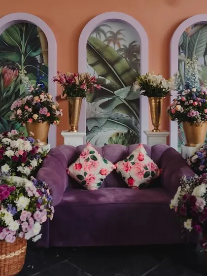 A plush purple sofa serves as a photo booth, surrounded by vibrant floral arrangements.