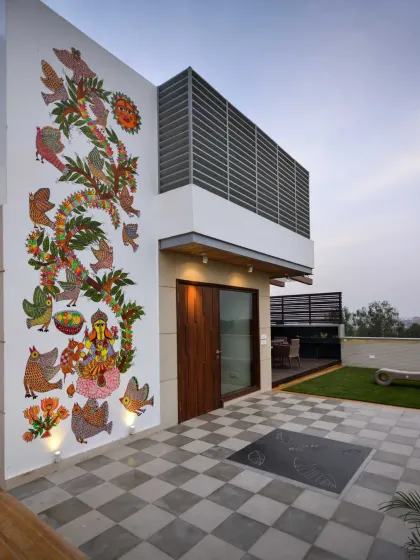 This terrace at the Kavyam Residence is a lively space for family gatherings. It blends tradition and modernity, featuring a vibrant Madhubani mural, a checkerboard stone floor, and a cozy seating area shaded by a wooden pergola.