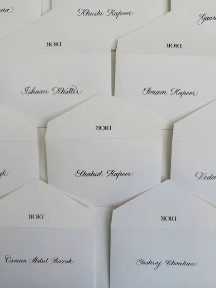 An overhead view of the calligraphed envelopes for Dior, featuring names like Sonam Kapoor and Shahid Kapoor. Each name is written with care and precision.