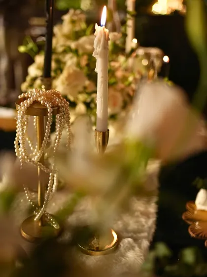 A romantic detail from the tablescape, featuring strands of pearls draped over a brass stand next to a flickering candle.