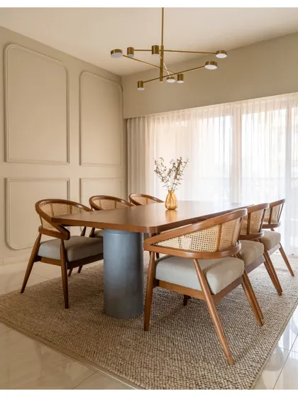 The dining area features a custom table with a concrete pedestal base, surrounded by classic wooden chairs with cane backs. The space is filled with natural light from the large window.