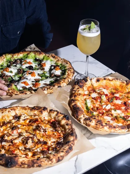 A table full of pizzas is a beautiful sight. Here you can see the variety I offer, from a classic tomato-based pie to a green pesto pizza and a creamy white pizza. There's a slice for every craving.