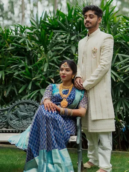 A regal portrait of a couple in traditional South Indian attire, seated on a bench in a lush garden.
