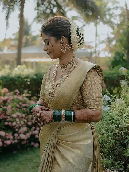 A serene moment captured in a garden setting. The bride wears a classic gold Kanchivaram with a matching embroidered blouse, a timeless choice for a muhurtham.
