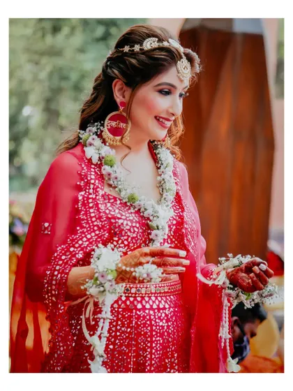 The bride is adorned with beautiful floral garlands for her Mehendi ceremony. This close-up shot highlights her personalized earrings and the delicate flower details.