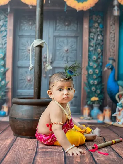 A sweet, seated pose of the baby dressed as Krishna, holding his flute. The entire setup is designed to be a playful and colorful tribute.