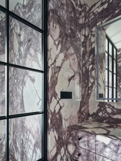 A truly dramatic bathroom, completely clad in a stunning purple-veined marble. The black-framed glass partition adds a modern, graphic contrast to the organic patterns of the stone.