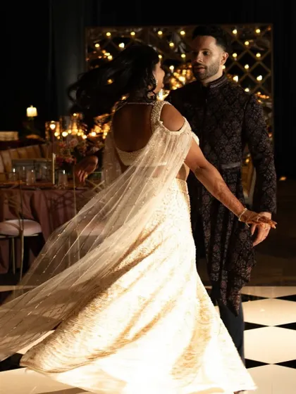 A reception look that is all about modern glamour. The bride's shimmering ivory lehenga and the groom's dark, textured sherwani create a stunning contrast on the checkered dance floor.