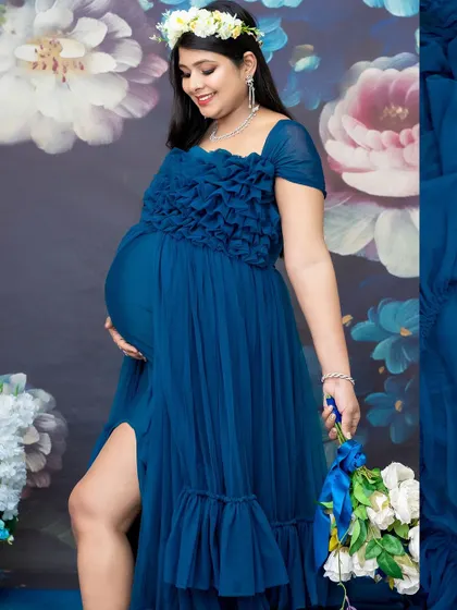 A close-up shot showcasing the details of the gown and the beauty of the baby bump. The floral backdrop adds a touch of romance to this elegant portrait.