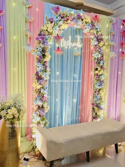 This pastel Mehendi setup creates a dreamy and modern aesthetic for your celebration. We use a soft palette of pastel drapes, a beautiful floral arch, hanging decor elements, and a custom 'Mehndi' neon sign to bring this vision to life.