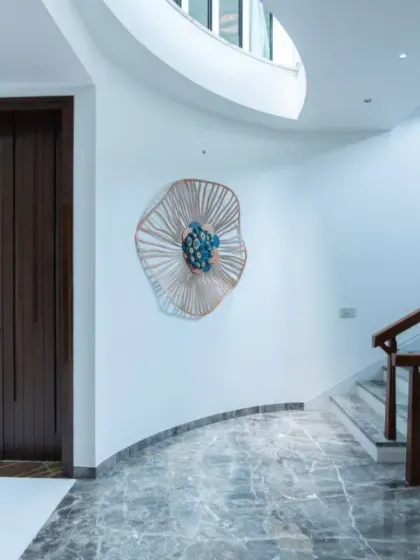 A curved wall guides the path towards a staircase in this entryway. The design uses soft curves, a mix of grey marble and white flooring, and a striking wall sculpture to create a memorable first impression.