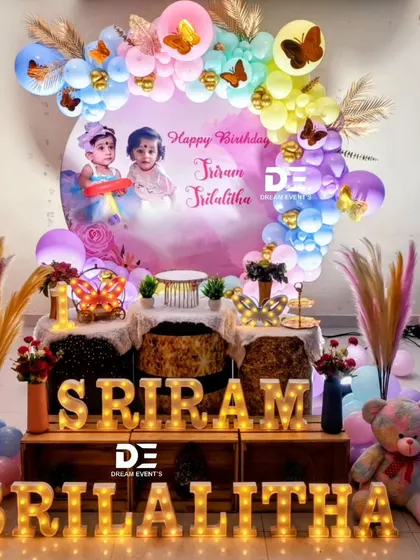 A colorful butterfly-themed birthday party for twins Sriram and Srilalitha. The backdrop features their photo surrounded by a rainbow balloon arch and butterfly accents.