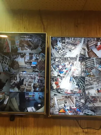 Two monitors displaying split-screen views from a comprehensive security system inside a retail store. This setup helps business owners monitor aisles, checkout counters, and storage areas simultaneously.