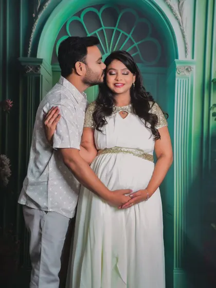 A sweet studio portrait where the partner gently kisses his wife's cheek. The soft green artistic backdrop adds a touch of elegance.