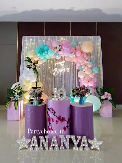 A beautiful pastel-themed birthday decoration with a light-up name display. The soft colors of the balloon arch and floral accents create a delicate and pretty setup for a girl's birthday.