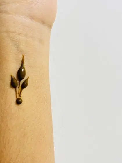 A tiny, simple leaf bud on the wrist, the perfect example of a minimal henna tattoo.