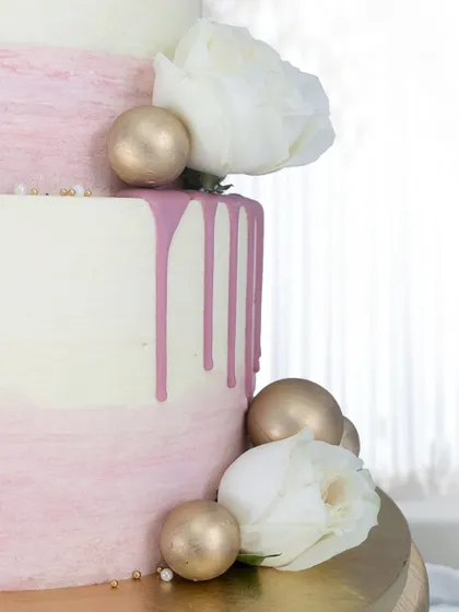 A detailed shot of the pink drip and golden spheres on this modern wedding cake. The combination of textures and colors creates a visually stunning effect.