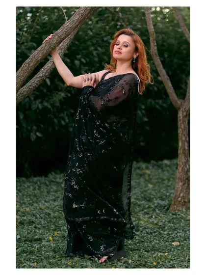 An elegant outdoor portrait in a black sequined saree. The natural setting provides a beautiful contrast to the glamorous attire.