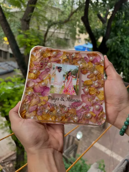 A beautiful shot of a square resin keepsake, showcasing the arrangement of pink and yellow petals, pearls, and the couple's photo. Every piece is a unique work of art.