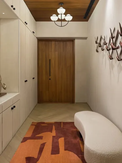 The private entrance lobby of the East Coast Residence is a long, gallery-like space. It features ample built-in storage and a sculptural coat rack, combining functionality with a strong design statement.
