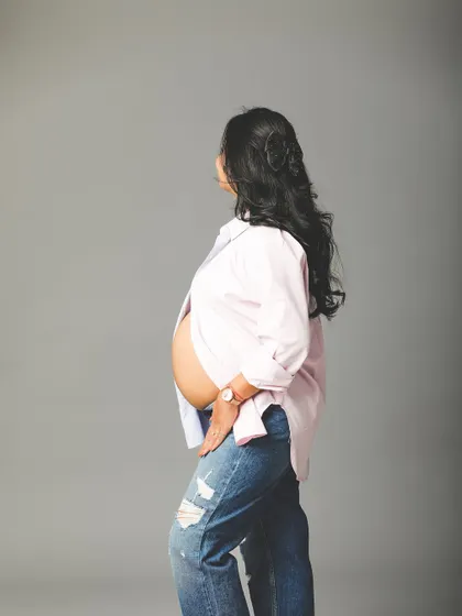 A side profile of a mom-to-be in a casual, unbuttoned shirt and jeans. This relaxed pose is perfect for showing the beautiful shape of the baby bump.