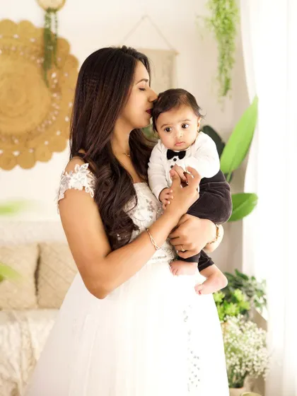 A mother gently kisses her baby's forehead in this tender portrait. The baby is dressed in a cute tuxedo onesie, ready for his family photos.