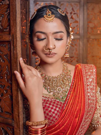 A serene moment captured in a classic bridal look. The soft makeup complements the bold red saree and intricate gold jewelry perfectly.