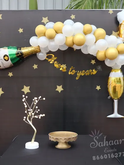 "Cheers to the years!" This fun bachelor party or milestone birthday backdrop features a champagne bottle balloon, a starry night theme, and a table for cake and gifts.