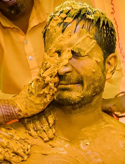 A close-up of the groom getting completely covered in turmeric paste. This shot captures the messy, tactile nature of the Haldi ceremony.
