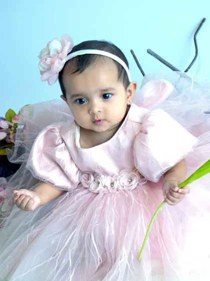A close-up of a baby girl in a beautiful pink dress, holding a flower and looking curiously at the camera. We focus on capturing these quiet, observant moments during our sessions.