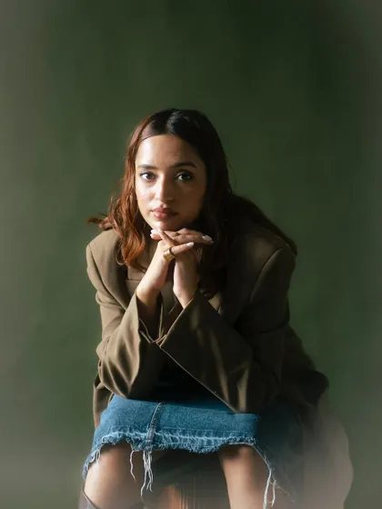 A seated portrait that combines a casual denim skirt with a formal blazer. The pose is thoughtful, and the soft, diffused lighting adds to the calm and collected mood of the shot.