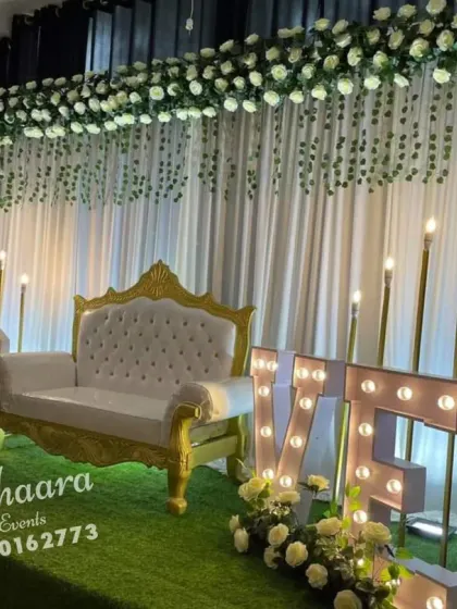 A romantic and elegant anniversary decoration. This setup features a white floral backdrop, an elegant settee, and large "LOVE" marquee letters, creating a perfect ambiance for celebrating a milestone.