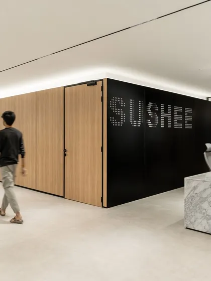 The reception area for Sushee infrastructure company features a bold, black perforated wall with the company's identity, set against natural wood and a solid marble desk. This combination of materials creates a first impression that is both sophisticated and progressively youthful.