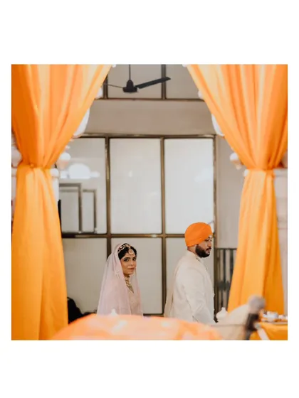 A beautifully framed shot of Suraj and Kajal during their ceremony, seen through the vibrant orange drapes of the Gurudwara.