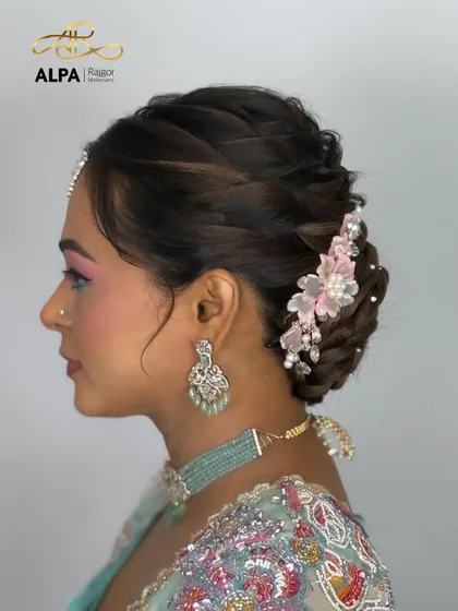 An elegant bun hairstyle featuring a delicate, handmade pink floral hair accessory with pearls, perfect for a reception or cocktail party.