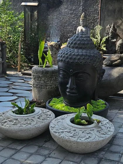 A beautiful arrangement of stone planters and a large black Buddha head, creating a striking contrast. These pieces are perfect for creating a Zen-inspired garden.