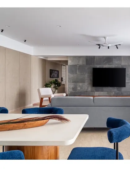 Another perspective of the living and dining space, showing the interplay between the cool tones of the sofa and chairs and the warm wood of the media unit in the background.