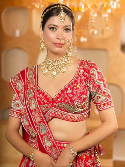 A full portrait of a bride in a traditional red lehenga, showcasing the detailed embroidery and the matching jewellery set available for rent.