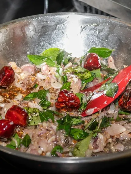 The vibrant colors of spices and herbs sizzling in a pan. This action shot from the Kari Apla kitchen captures the aromatic base of a South Indian dish.