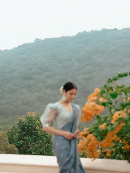 A soft-focus outdoor shot from a lookbook. The model in a saree is set against a hazy mountain backdrop, creating a dreamy and romantic atmosphere.