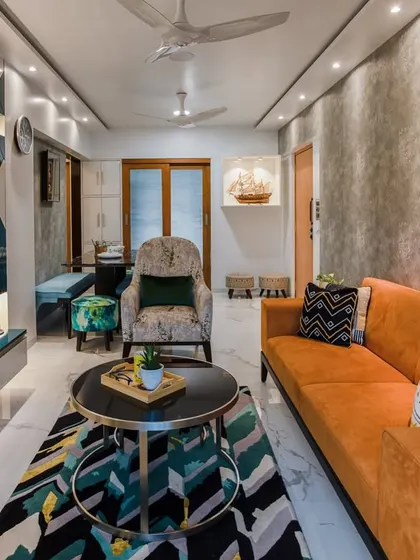 This living room is a perfect play of colors, with a bold orange sofa, a geometric-patterned rug, and vibrant abstract art against a textured grey wall.